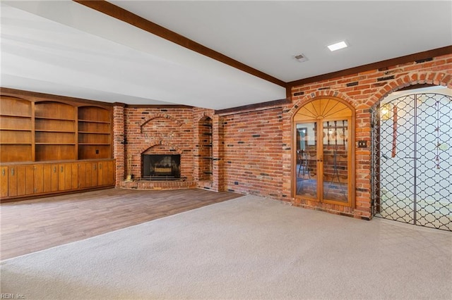 unfurnished living room featuring beam ceiling, carpet flooring, a fireplace, and brick wall