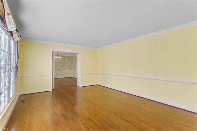 empty room featuring wood finished floors, baseboards, visible vents, crown molding, and a chandelier