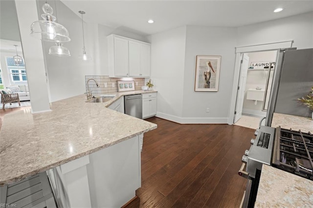 kitchen with dark wood finished floors, a peninsula, stainless steel appliances, a sink, and backsplash