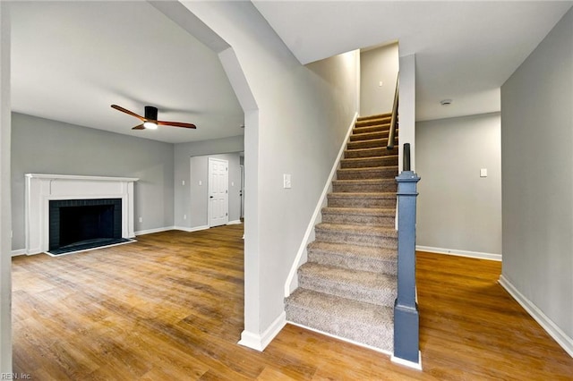staircase with a fireplace, baseboards, a ceiling fan, and wood finished floors