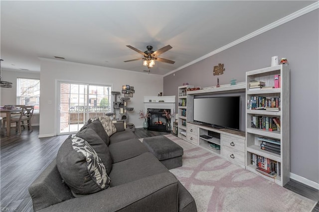 living area with ceiling fan, wood finished floors, baseboards, and ornamental molding