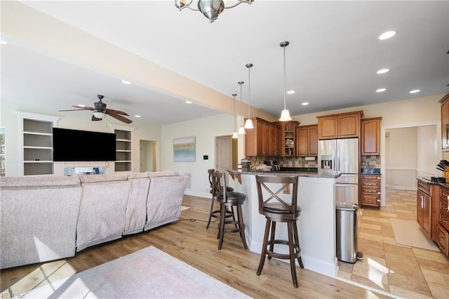 kitchen with a peninsula, a breakfast bar, glass insert cabinets, stainless steel fridge with ice dispenser, and backsplash