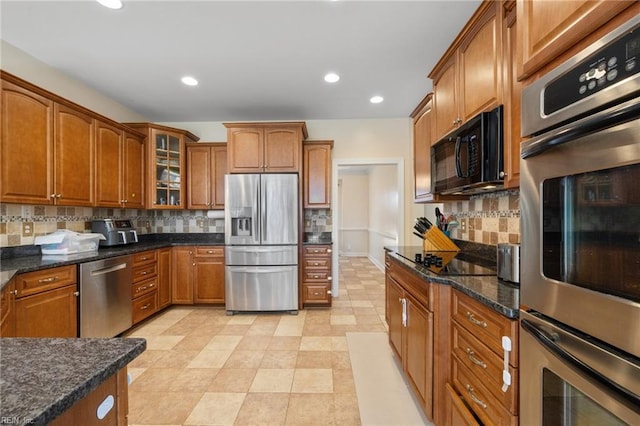 kitchen featuring backsplash, dark stone counters, black appliances, brown cabinetry, and glass insert cabinets