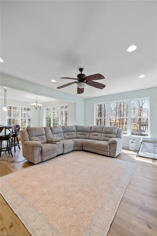 living area featuring wood finished floors, a healthy amount of sunlight, and ceiling fan with notable chandelier