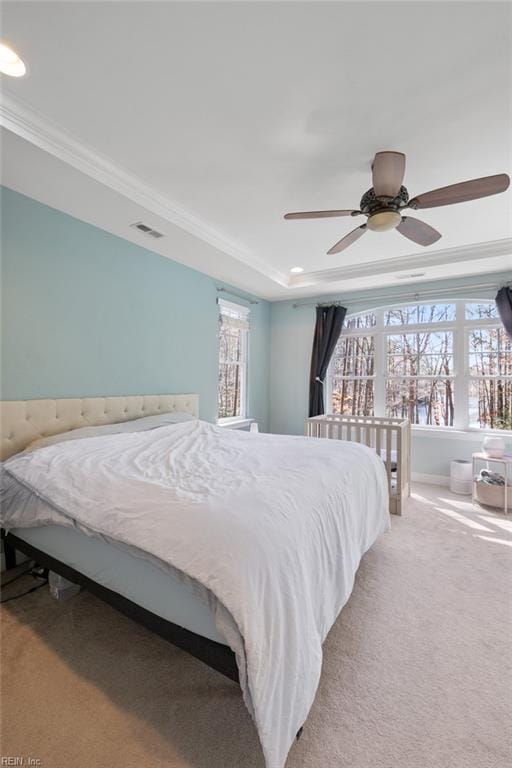 carpeted bedroom with a ceiling fan, a raised ceiling, ornamental molding, and visible vents