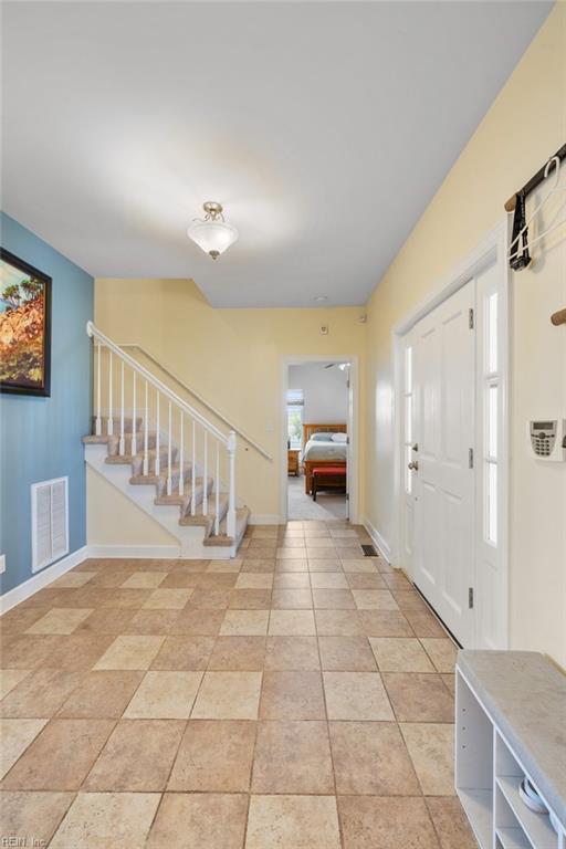 foyer entrance with baseboards, stairs, visible vents, and light tile patterned floors