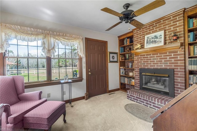 sitting room with baseboards, built in shelves, carpet floors, ceiling fan, and a brick fireplace