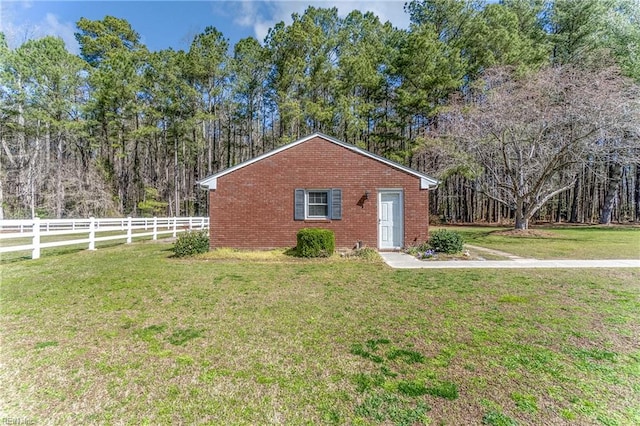 view of side of property featuring brick siding, fence, and a lawn