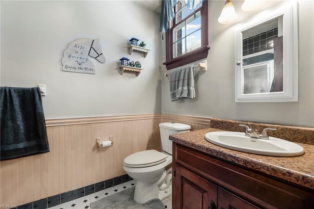 bathroom with a shower, a wainscoted wall, vanity, and toilet