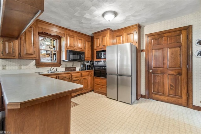 kitchen with black appliances, brown cabinetry, a peninsula, and wallpapered walls