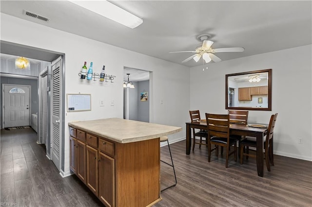 kitchen featuring a ceiling fan, dark wood-style floors, visible vents, a breakfast bar, and light countertops