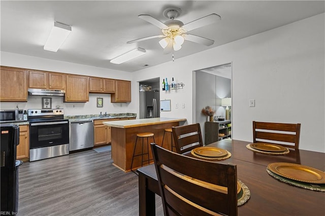 kitchen featuring a ceiling fan, a kitchen island, dark wood finished floors, under cabinet range hood, and appliances with stainless steel finishes