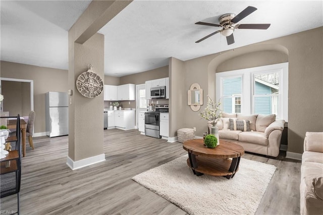 living room with baseboards, light wood-type flooring, a textured wall, and ceiling fan