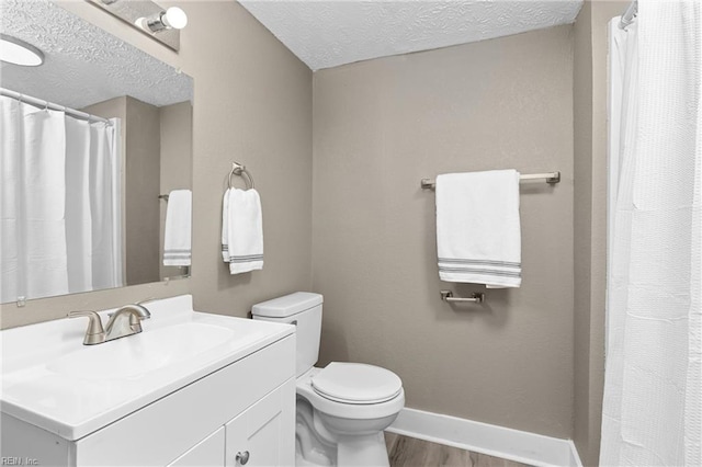 bathroom featuring baseboards, toilet, vanity, wood finished floors, and a textured ceiling