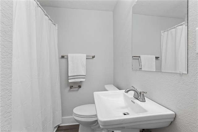 bathroom featuring toilet, a sink, a textured ceiling, wood finished floors, and a shower with shower curtain