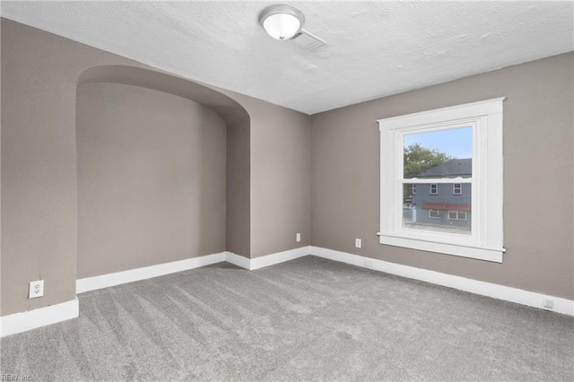 carpeted empty room featuring arched walkways, a textured ceiling, and baseboards
