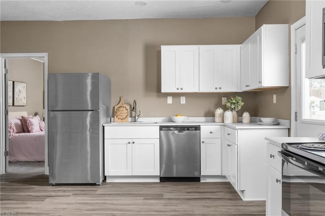 kitchen featuring light wood-type flooring, a sink, white cabinetry, stainless steel appliances, and light countertops