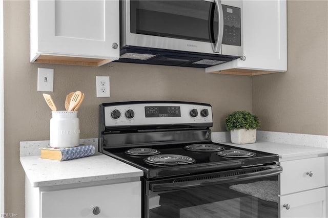 kitchen with white cabinetry, stainless steel microwave, light stone countertops, and electric range oven