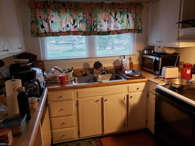 kitchen with a sink, stainless steel microwave, range with electric stovetop, white cabinets, and light countertops