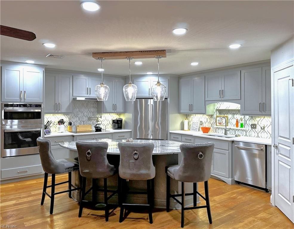 kitchen featuring visible vents, a kitchen island, light wood-type flooring, stainless steel appliances, and a sink