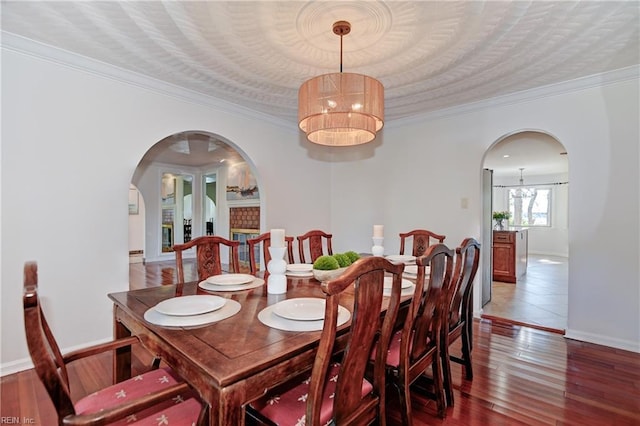 dining space with hardwood / wood-style floors, baseboards, arched walkways, a textured ceiling, and crown molding