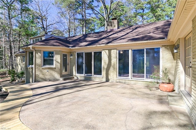 back of property featuring brick siding, a chimney, and a patio