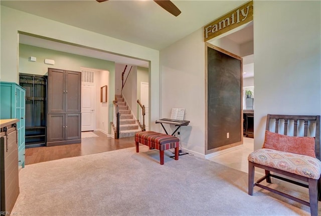 living area with stairway, light carpet, baseboards, and a ceiling fan