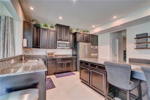 kitchen with a breakfast bar, a sink, recessed lighting, appliances with stainless steel finishes, and light stone countertops