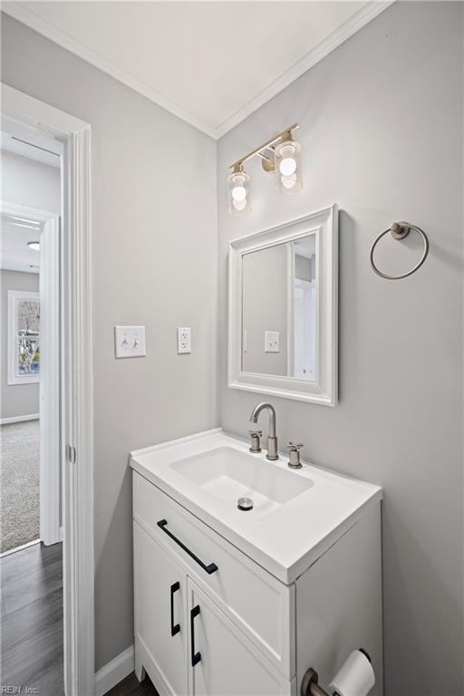 bathroom featuring vanity, crown molding, baseboards, and wood finished floors