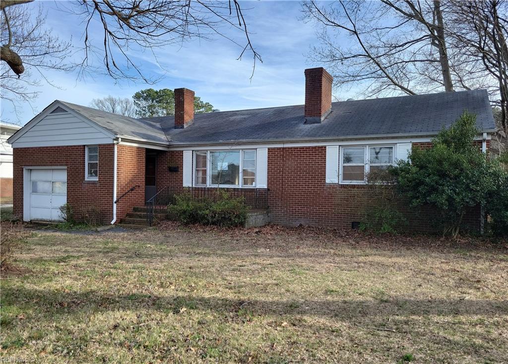 ranch-style home with an attached garage, a chimney, a front lawn, and brick siding