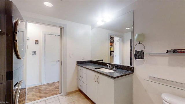 bathroom featuring tile patterned flooring, vanity, toilet, stacked washing maching and dryer, and baseboards
