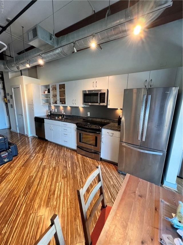kitchen featuring dark countertops, wood finished floors, a towering ceiling, and appliances with stainless steel finishes