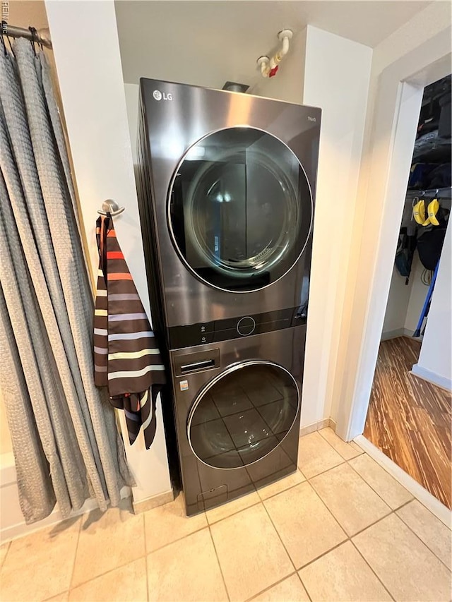 laundry area with laundry area, baseboards, stacked washing maching and dryer, and tile patterned flooring
