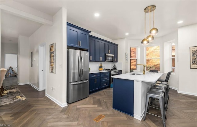 kitchen with light countertops, blue cabinets, a sink, an island with sink, and appliances with stainless steel finishes