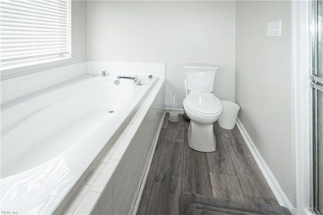 full bathroom with toilet, a garden tub, baseboards, and wood finished floors