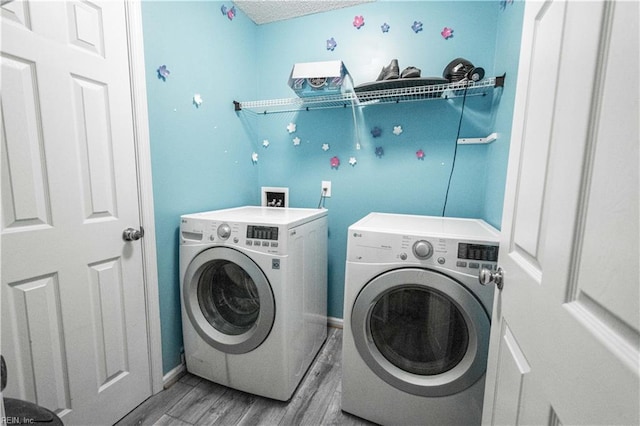 clothes washing area featuring washing machine and dryer, laundry area, baseboards, and wood finished floors