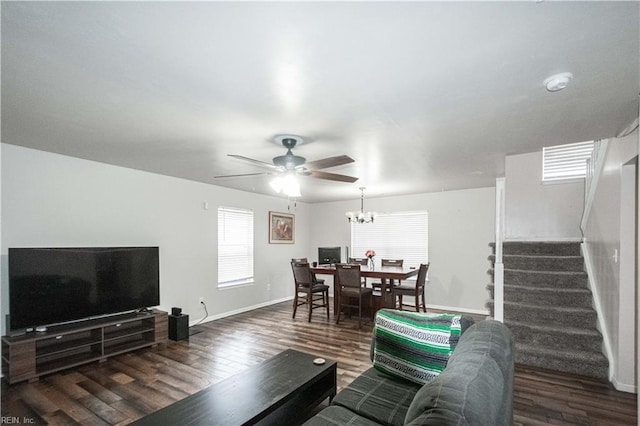 living area featuring stairs, ceiling fan with notable chandelier, baseboards, and wood finished floors