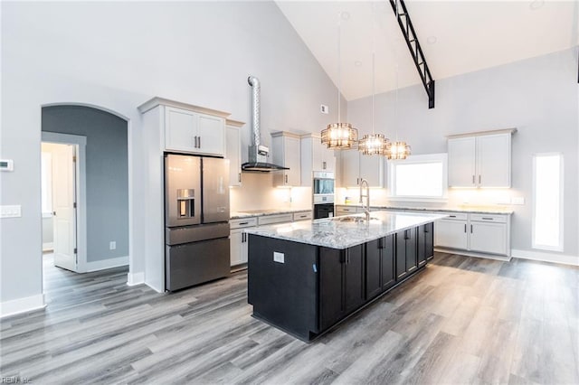 11AC Glass Rd, Hayes, VA 23072 - kitchen featuring a kitchen island with sink, arched walkways, a sink, wall chimney range hood, and stainless steel fridge
