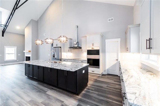 11AC Glass Rd, Hayes, VA 23072 - kitchen with wall chimney range hood, high vaulted ceiling, an island with sink, stainless steel appliances, and white cabinetry