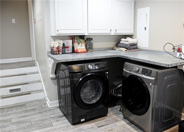 clothes washing area with cabinet space, washer and dryer, light wood finished floors, and electric panel