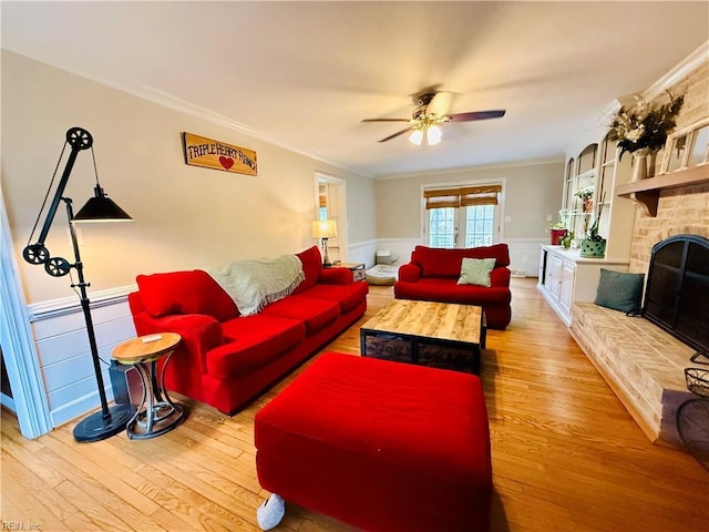 living area with a wainscoted wall, ceiling fan, wood finished floors, ornamental molding, and a stone fireplace