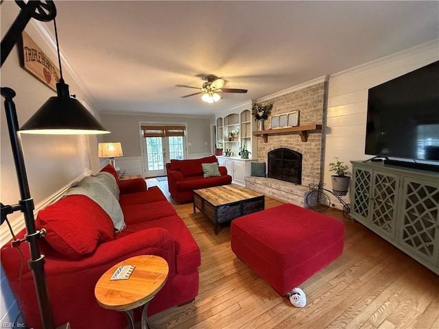 living room featuring ornamental molding, wood finished floors, a ceiling fan, and a brick fireplace