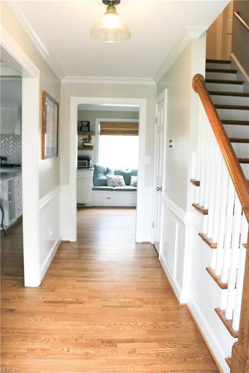 corridor featuring ornamental molding, light wood-style flooring, stairway, and wainscoting