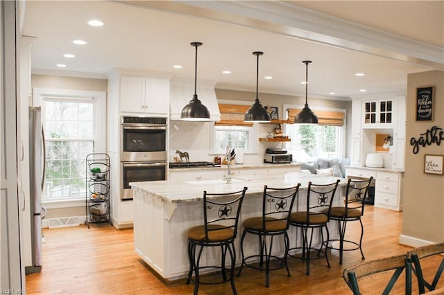kitchen with white cabinetry, stainless steel appliances, ornamental molding, and light wood finished floors