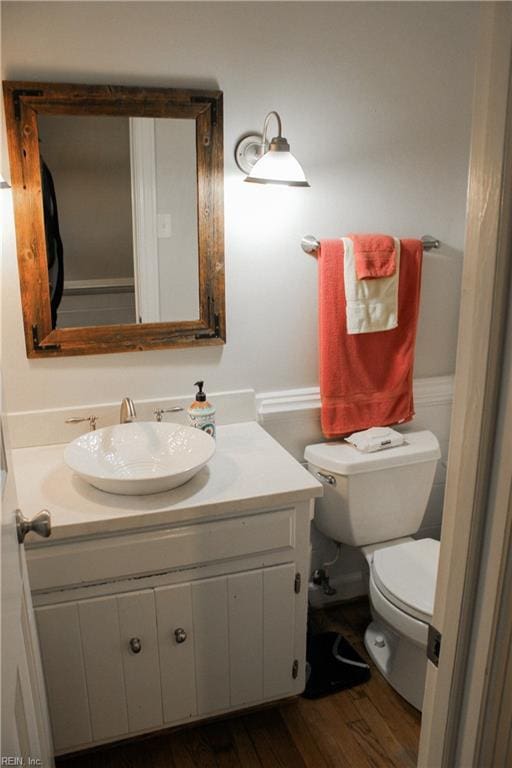 half bath with wood finished floors, toilet, and vanity