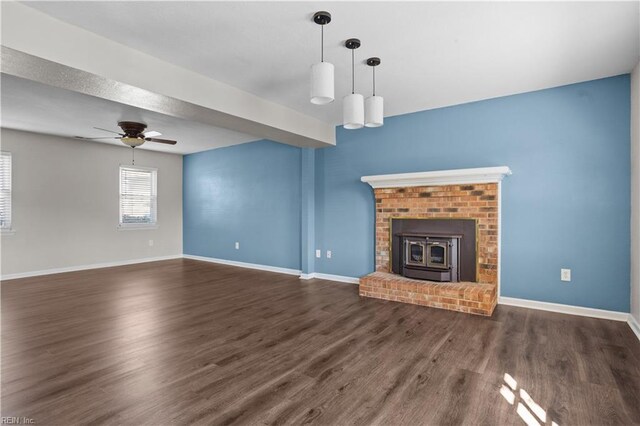 unfurnished living room with baseboards, wood finished floors, a wood stove, and a ceiling fan