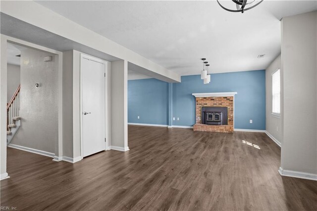 unfurnished living room with a brick fireplace, baseboards, stairway, and wood finished floors