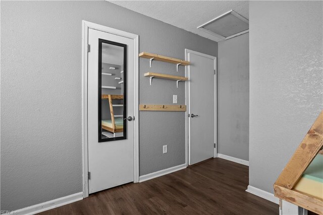 interior space featuring a textured wall, baseboards, attic access, and wood finished floors