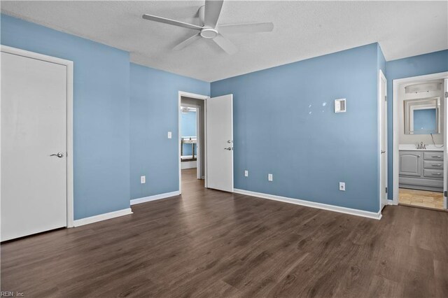 unfurnished bedroom with a textured ceiling, baseboards, connected bathroom, dark wood finished floors, and a sink