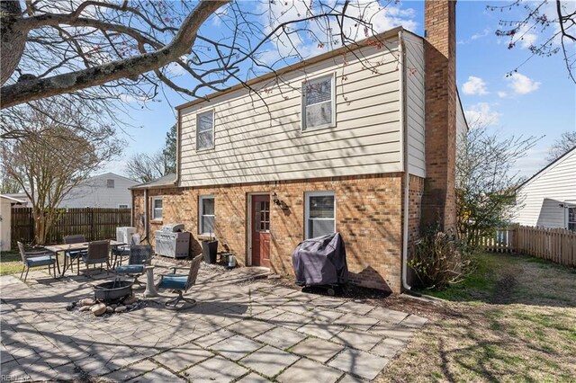rear view of property featuring a patio, a chimney, a fenced backyard, brick siding, and a fire pit